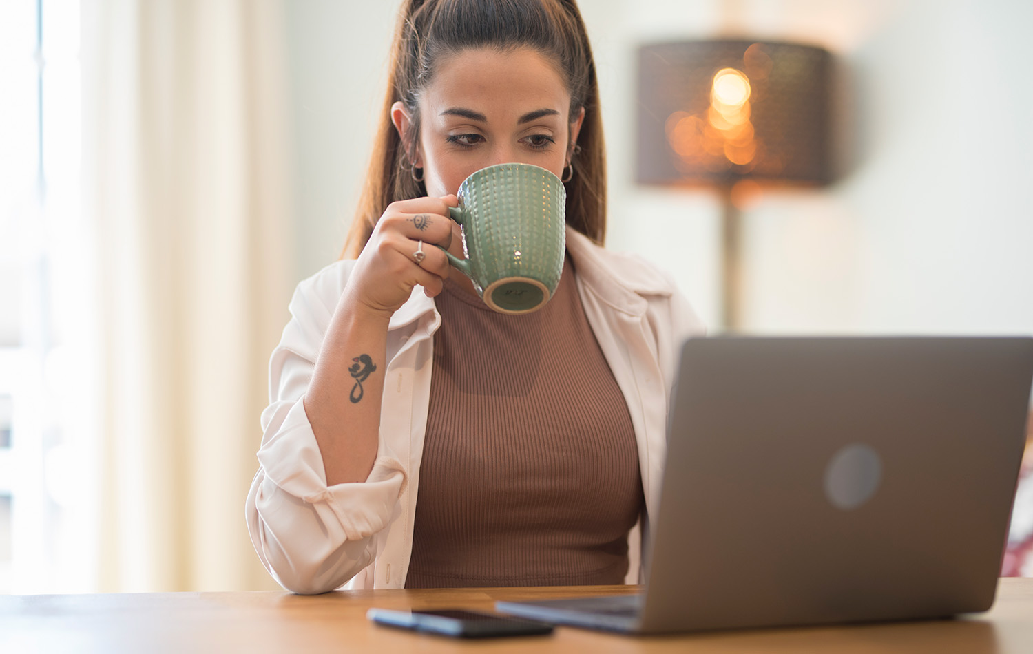 woman reading from a laptop computer drinking from a mug